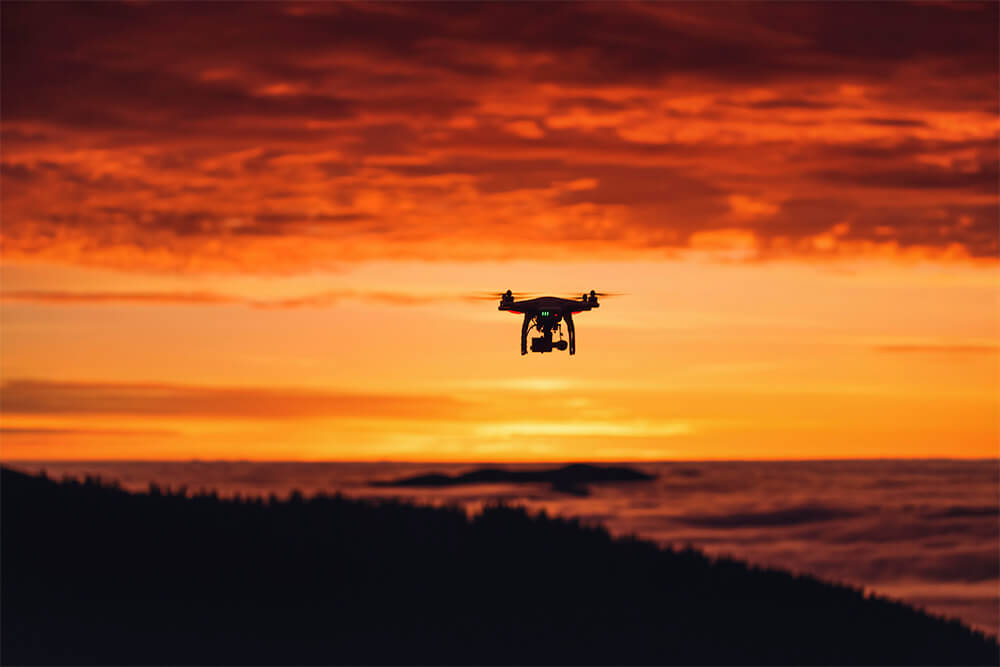 An Opus Interactive blog post image about Tech Revolution, the image depicts a picture of a drone flying over a forest during a sunset.