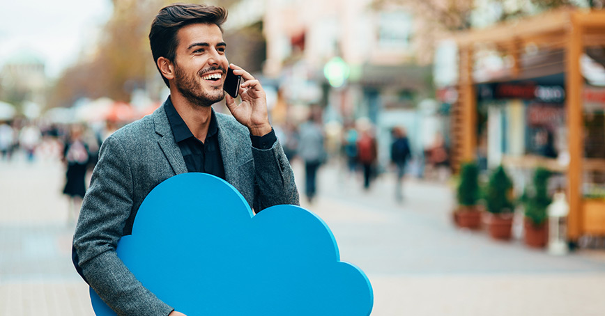 A blog image depicting a man on a phone walking down the street carrying a giant blue cloud icon under his free arm.