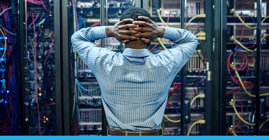 A blog post image depicting a man holding his hands to his head at a loss as he confronts a messy server room, seemingly unknowing where to start.