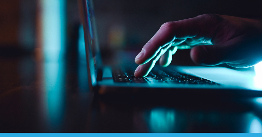 A blog post image depicting a close up shot of a man typing on his laptop in a dimly lit room.