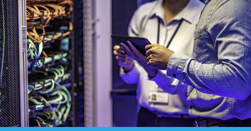 A blog post image depicting a close up shot of two IT technicians accessing a server rack with a tablet. Presumably routine maintenance.